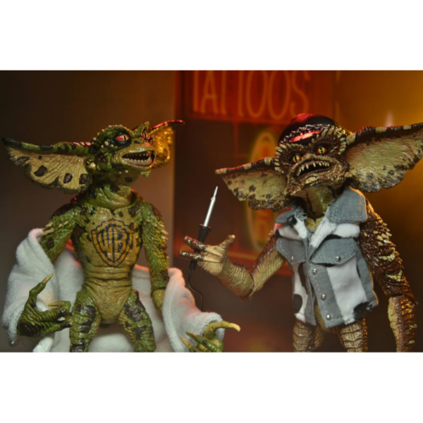 Neca presenta este set de 2 figuras de Gremlins en el éstos asaltan un salón de tatuajes. Esta escena se basa en la divertidísima secuela de Warner Bros, "Gremlins 2: La nueva generación". Cada figura mide unos 18 cms e incluye manos intercambiables, una máquina para hacer tatuajes, un mazo, unas gafas de sol, una fusta, una toalla de tela y un chaleco tejano.